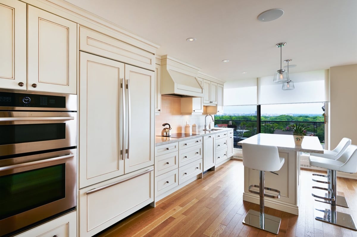 Cream cabinets with range hood and island and white barstools kitchen condo renovation in Toronto